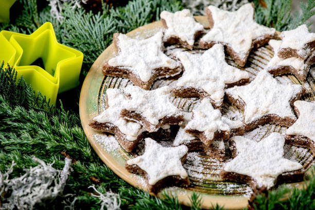 Homemade star shape cocoa almond cookies with white glaze and icing sugar. On ceramic plate with xmas stars cookies cutters on thuja branches. Close up. (Photo by: Natasha Breen/REDA&CO/Universal Images Group via Getty Images)