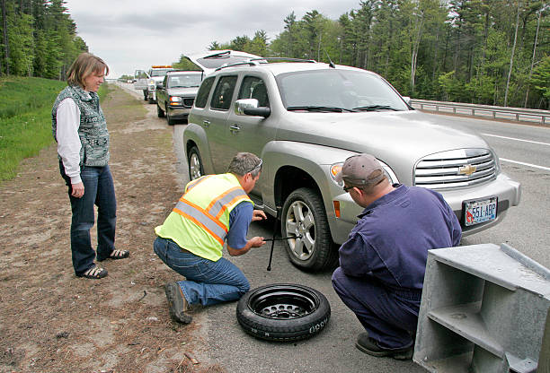 Jill Brady/Staff Photographer: Lauren DeLong, left, of York watches while Mike DeSimone of the Maine Turnpike Courtesy Patrol, center, and Rich Johnson of Wells help change a flat tire just before exit 19, southbound, in Wells Friday afternoon. DeLong was the second driver to hit a large piece of metal on the highway which was picked up shortly afterwards by the Maine Turnpike Authority. *for Tess story* (Photo by Jill Brady/Portland Press Herald via Getty Images)